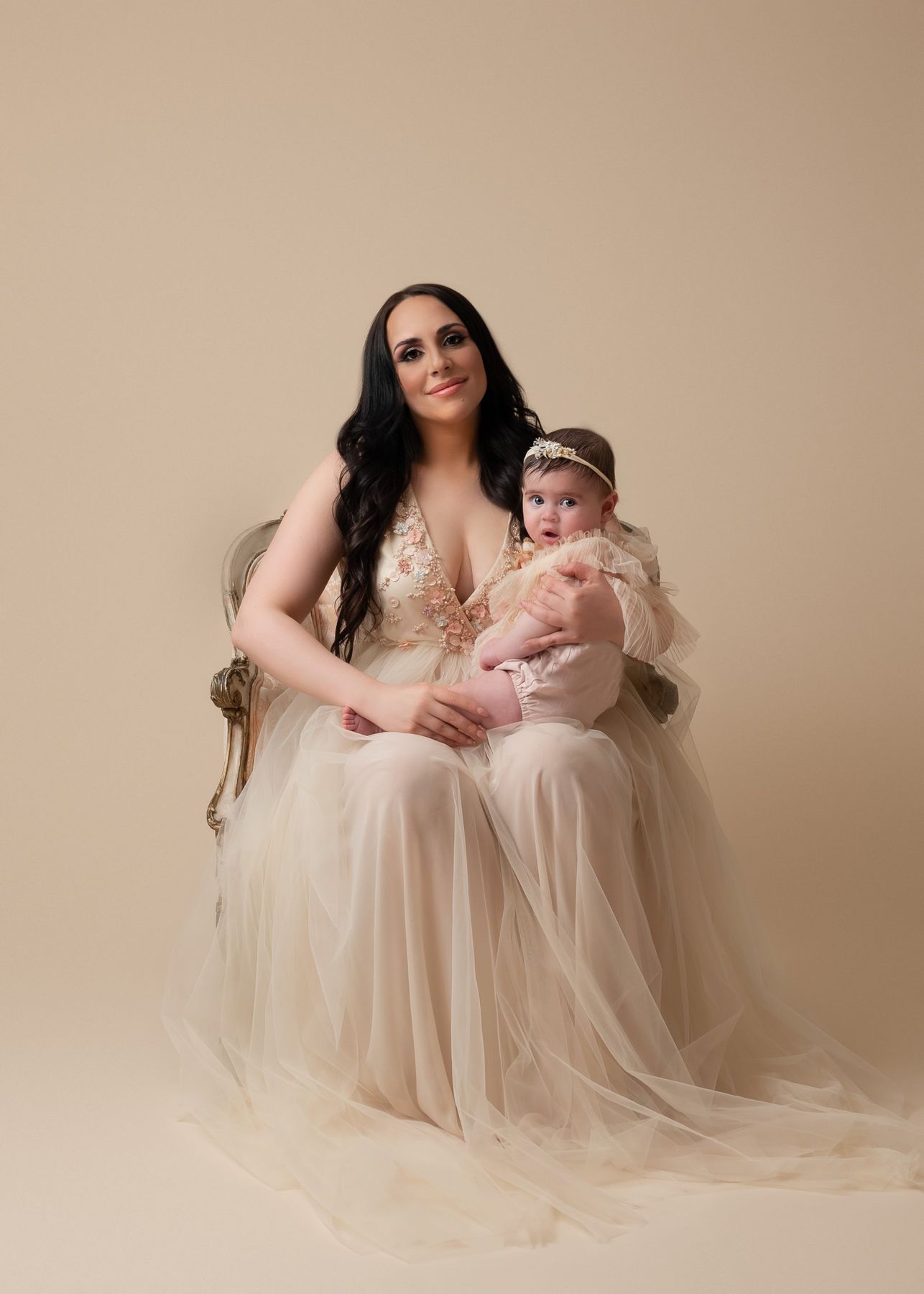 Mother in a tulle gown with her baby on an antique chair