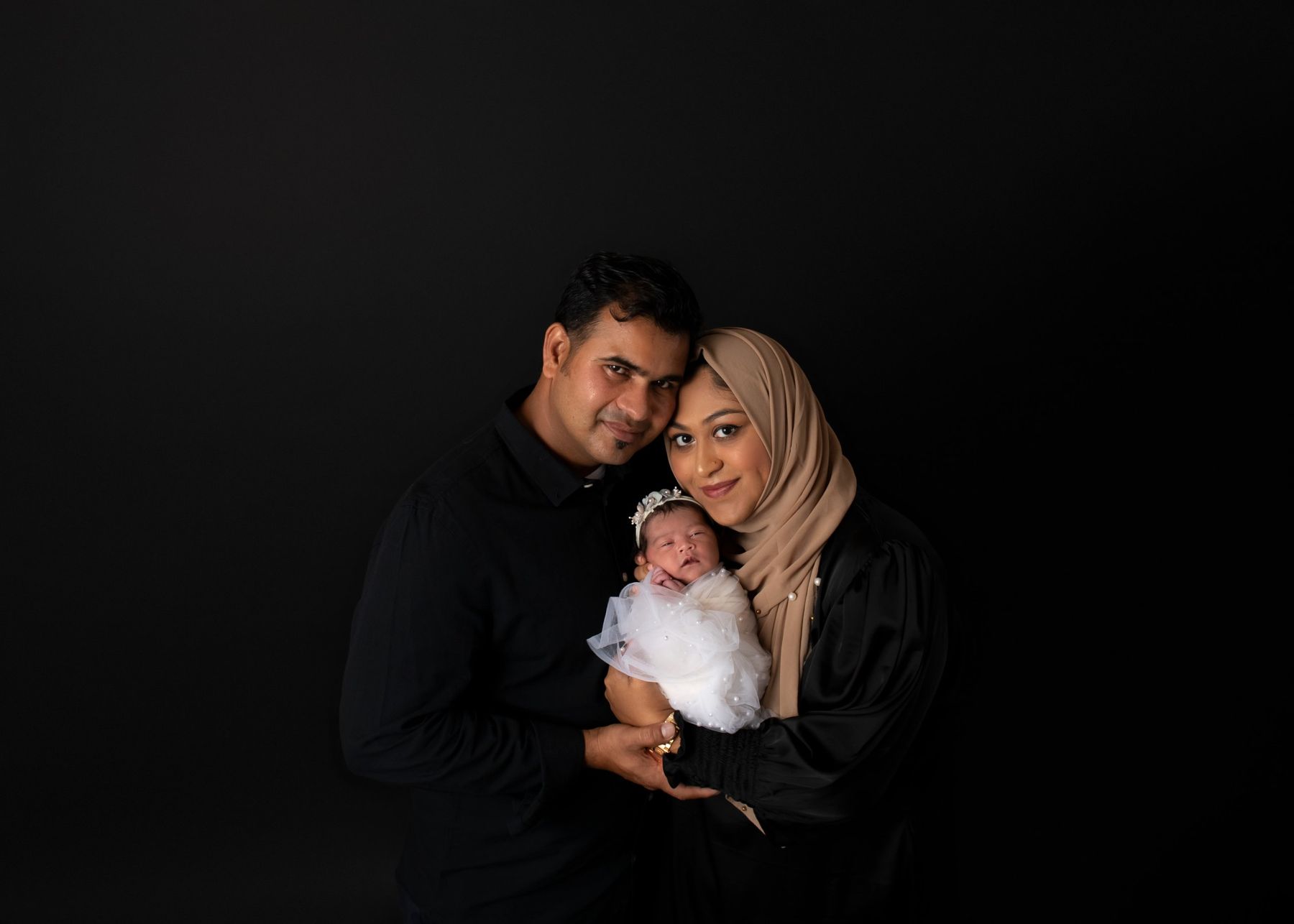 Parents with their newborn in pearl tulle on black